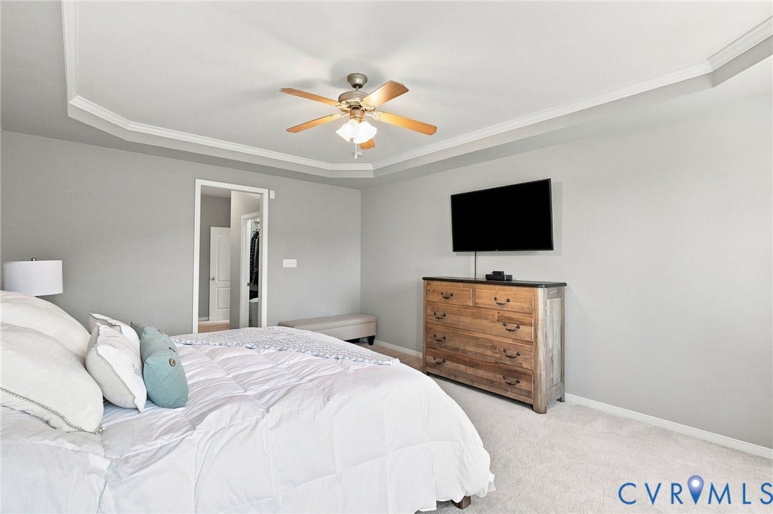 Tray ceiling with crown molding, ceiling fan, carpet flooring, and a wall-mounted television