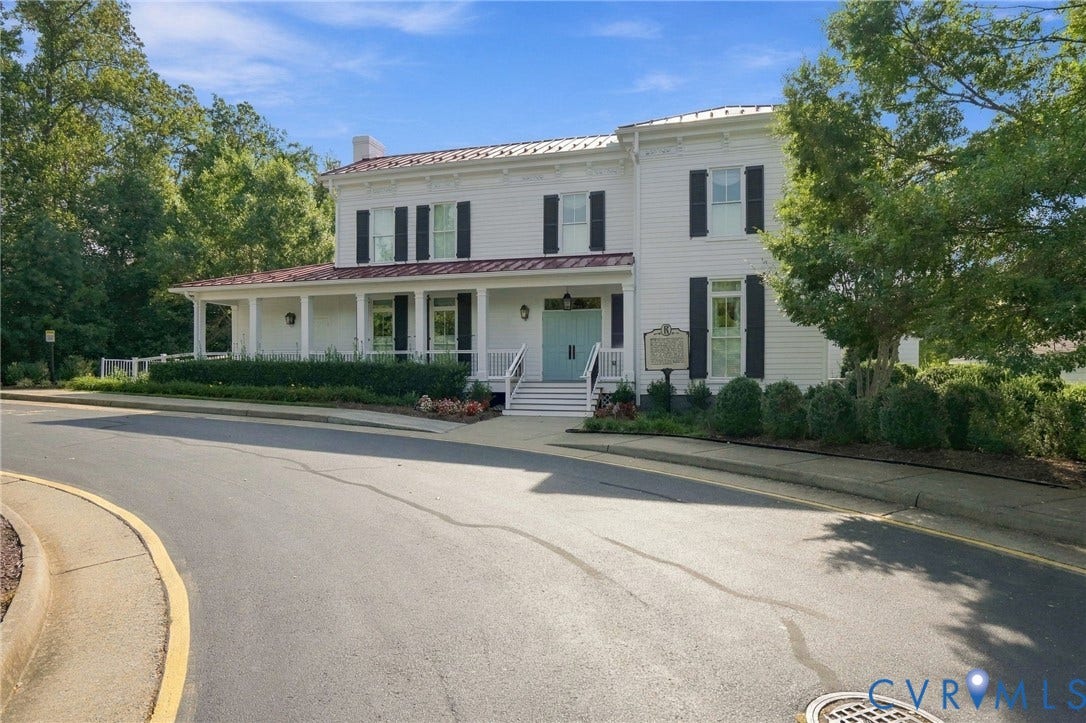 White clapboard exterior with black louvered shutters, a covered front porch, light blue double entry doors, and a copper-finish roof