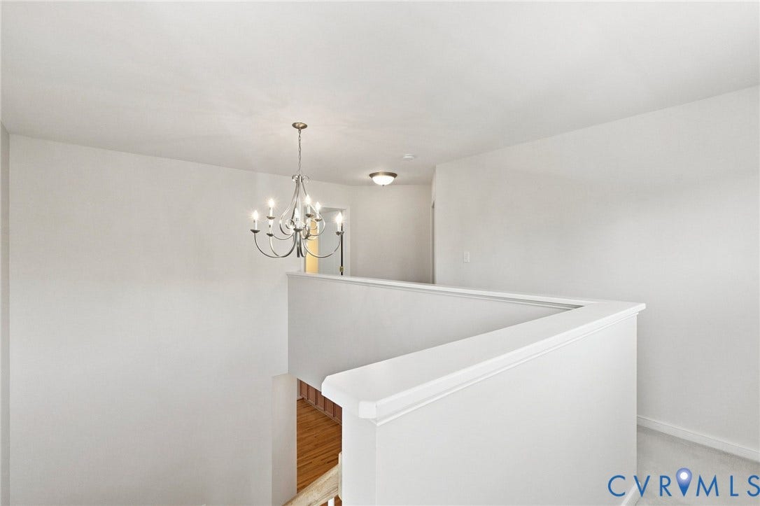 Upper-level landing with a chandelier, half-wall railing, and recessed lighting