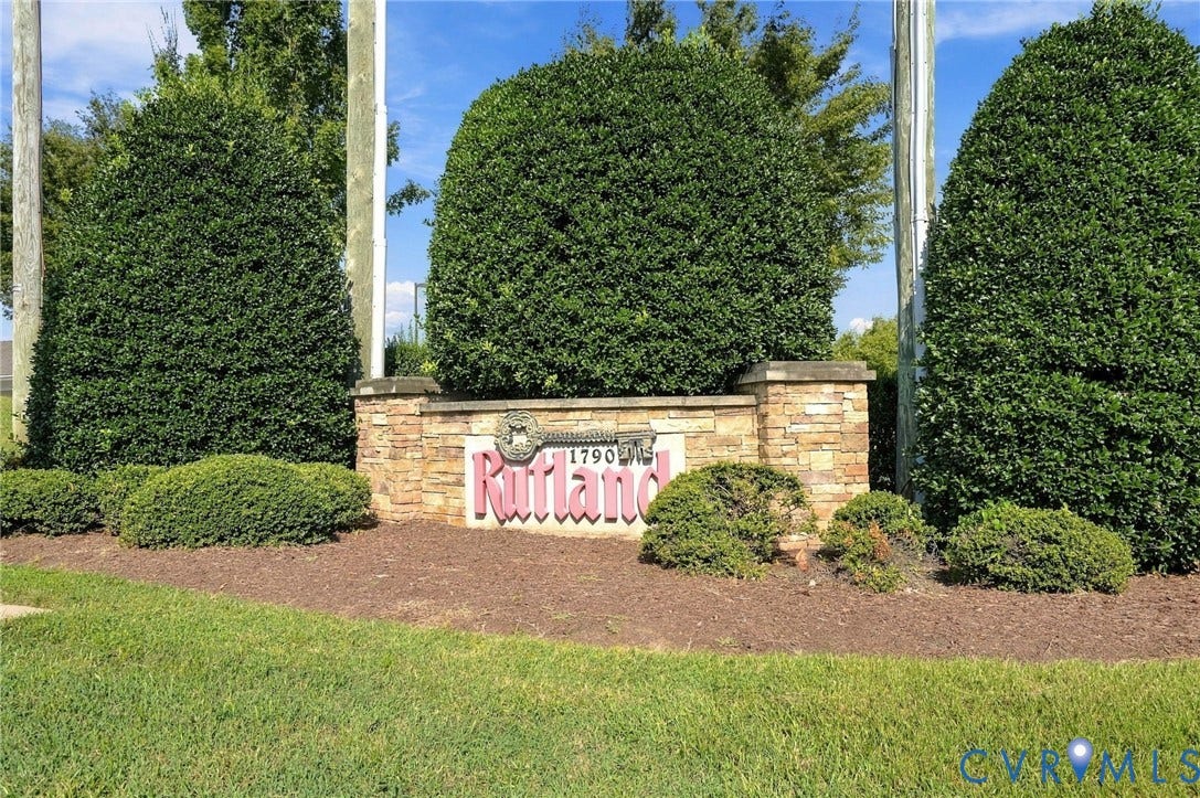 Stone-clad entry monument with a decorative plaque, surrounded by manicured shrubbery and a grass lawn