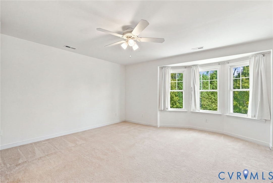 Expansive room featuring a bay window with three large windows, a ceiling fan with integrated lighting, and neutral carpeting