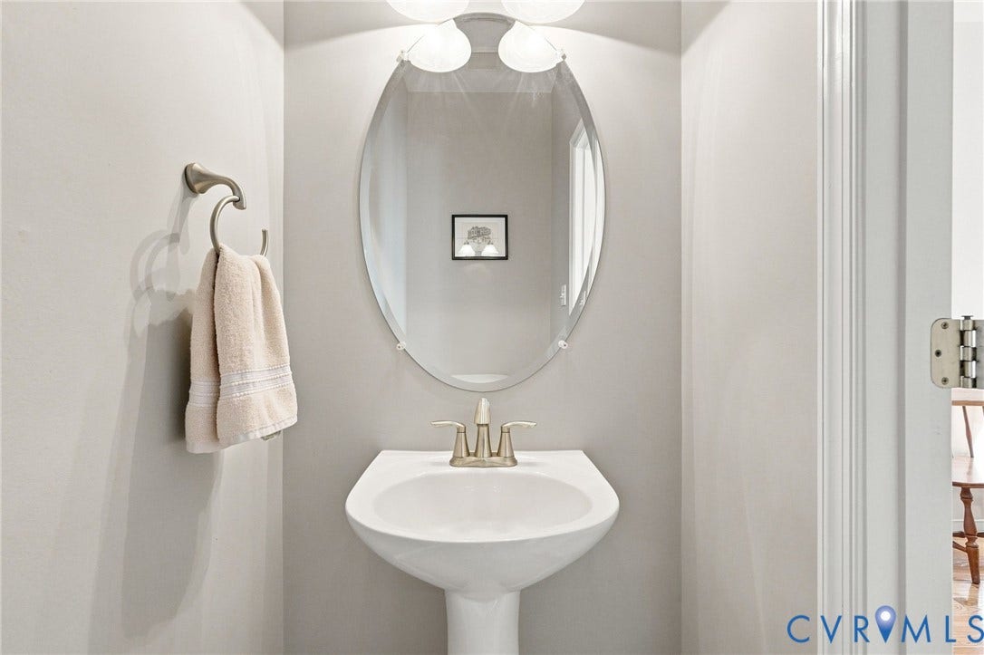Pedestal sink with brushed nickel faucet, oval mirror, and wall-mounted light fixture