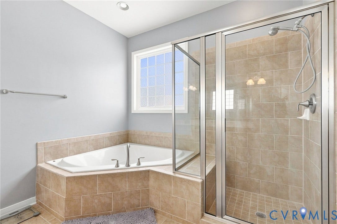 Corner soaking tub, fully tiled shower enclosure with glass doors, tiled flooring, recessed ceiling lighting, and a frosted window