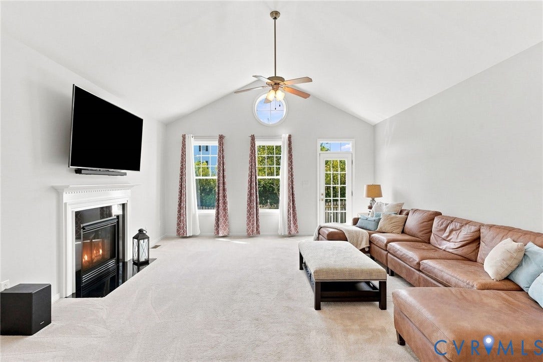 Vaulted ceiling with a ceiling fan, fireplace with a mantle, multiple windows, and exterior door