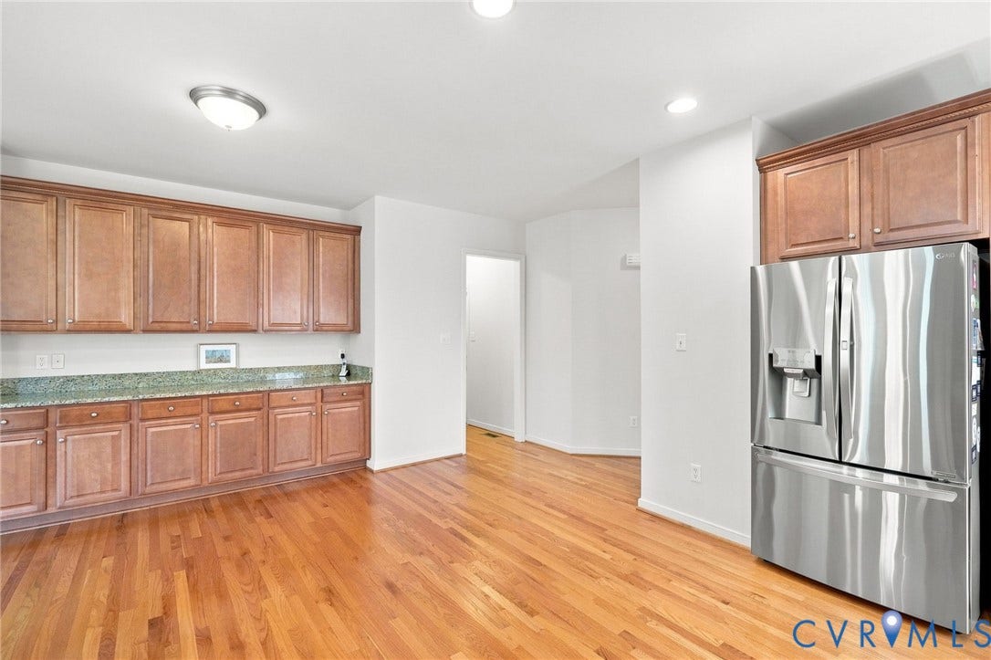 Kitchen featuring wood-finish flooring, recessed lighting, upper and lower wood cabinetry, stone countertops, and a stainless steel refrigerator