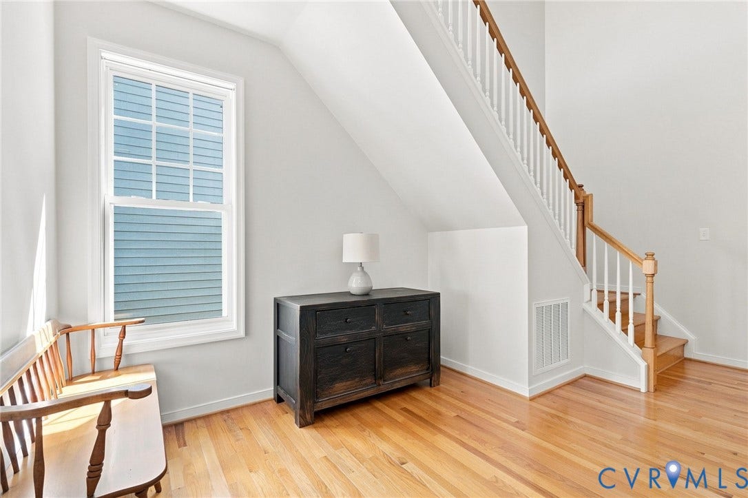 Hardwood flooring, painted white walls, wood staircase with white balusters, and a large window