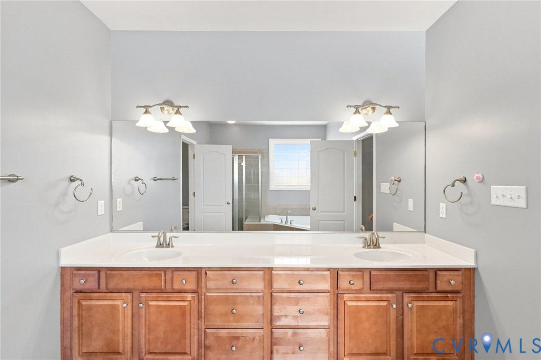 Dual vanity with wood-finish cabinetry, integrated sinks, white countertop, and expansive mirror