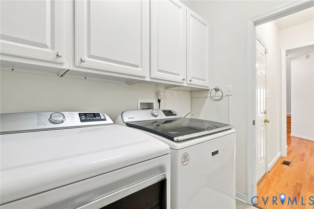 White cabinetry with silver hardware, full-size washer and dryer, and light wood-finish flooring