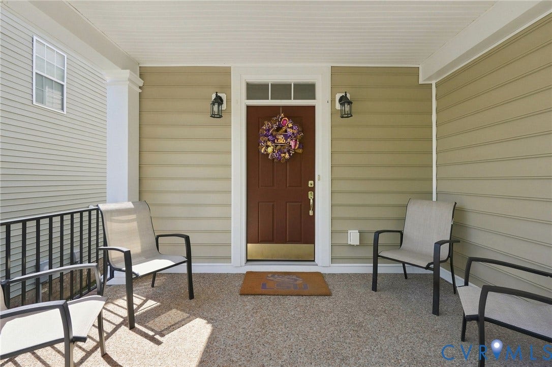 Covered front porch featuring a brown entry door with transom window, two wall-mounted lanterns, and a textured concrete surface