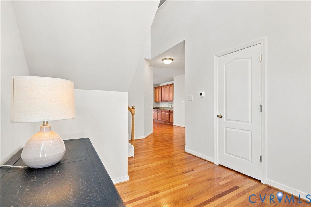Hardwood flooring extending through the hallway, white interior doors, and a wood-finish staircase railing