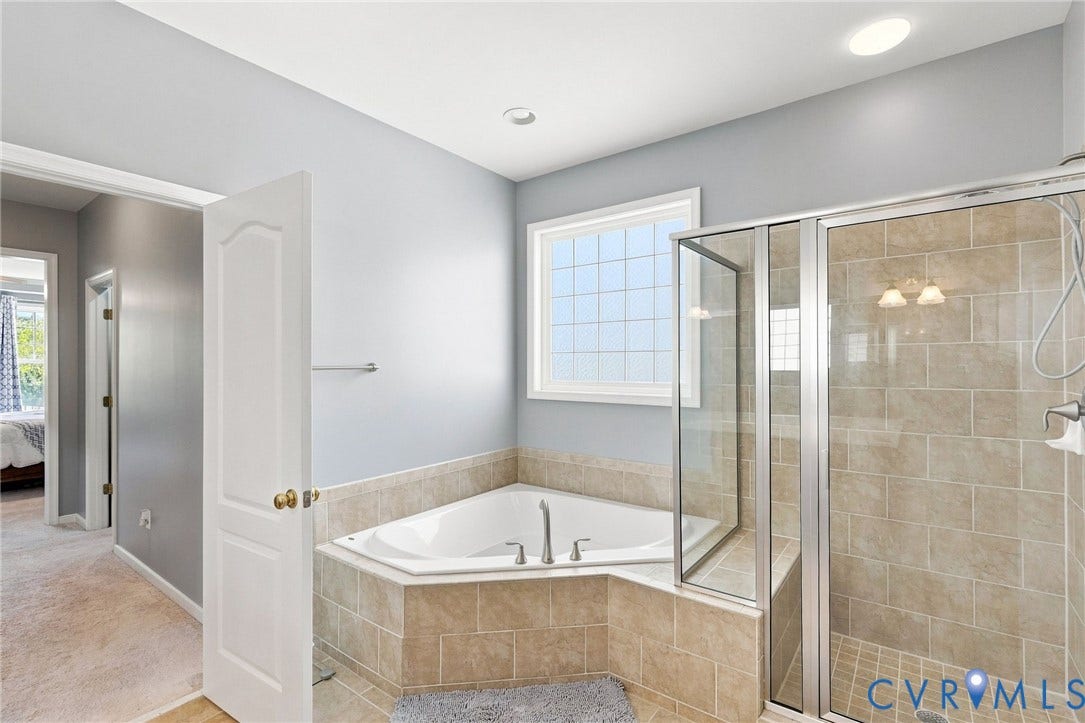 Corner soaking tub with tile surround, glass-enclosed shower with tile walls, overhead recessed lighting, and a multi-pane window