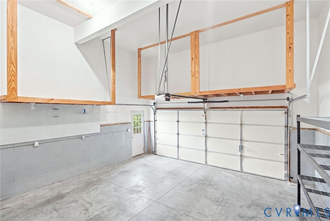 Concrete floor, built-in overhead storage shelving, side entry door, pegboard wall, and integrated garage door opener