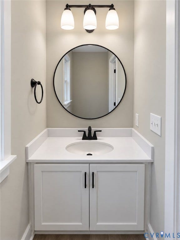 1010 Johnson Road, Mineral, VA 23117 White vanity with an integrated sink and matte black faucet, featuring a round black-framed mirror, three-light fixture, and wood-finish flooring