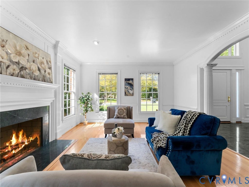 Hardwood flooring, stately fireplace with dark stone surround, decorative crown molding, double windows, and arched entryway with fluted columns