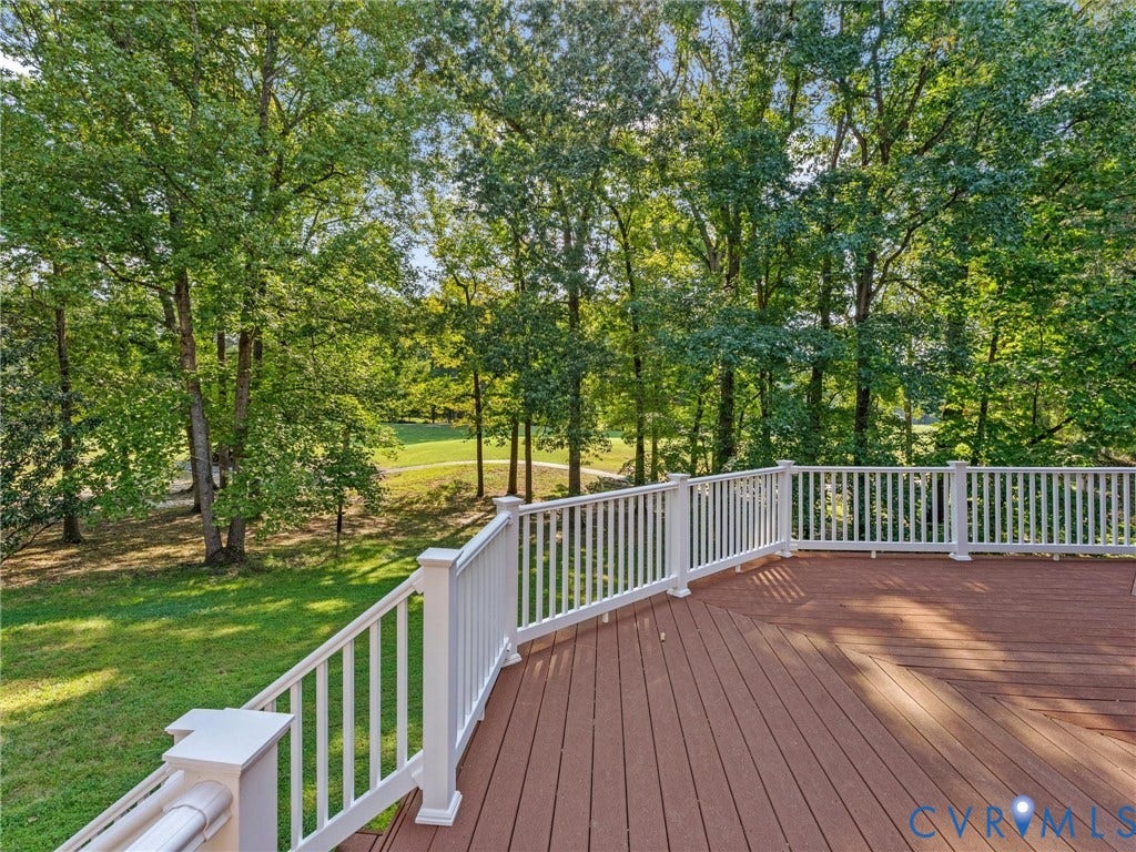 Spacious outdoor deck with composite decking and white railing, surrounded by mature trees and lush green landscaping