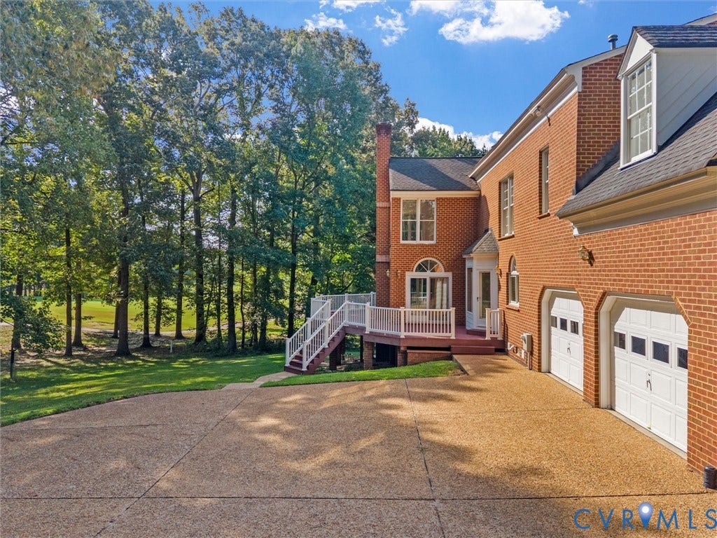 Brick exterior with white trim, multi-car garage, expansive driveway, elevated deck, and mature trees