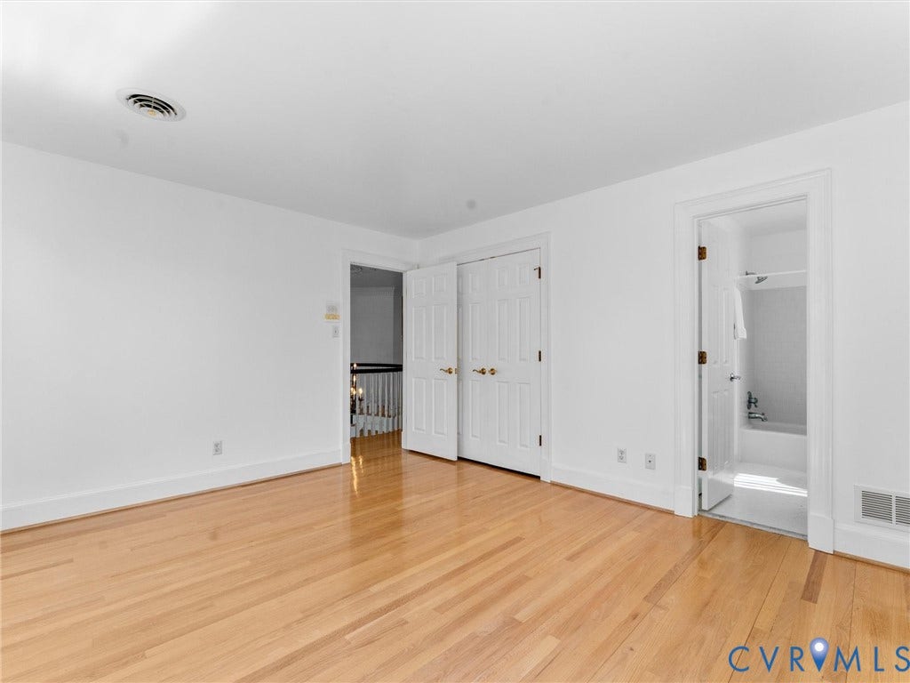 Guest bed w/ en suite bath Hardwood flooring, white walls, double bi-fold closet doors, and an en-suite bathroom with a built-in tub