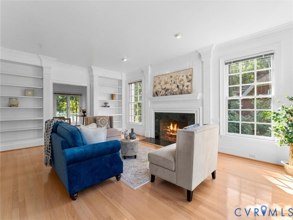 Hardwood flooring, fireplace with a dark stone surround, white mantel, built-in shelving, and large windows