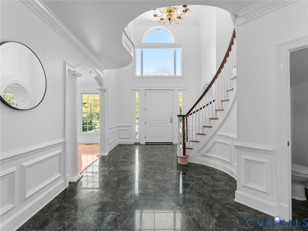 Two-story foyer with high ceilings, featuring a curved staircase with wood-finish handrails, marble-look flooring, and a decorative archway