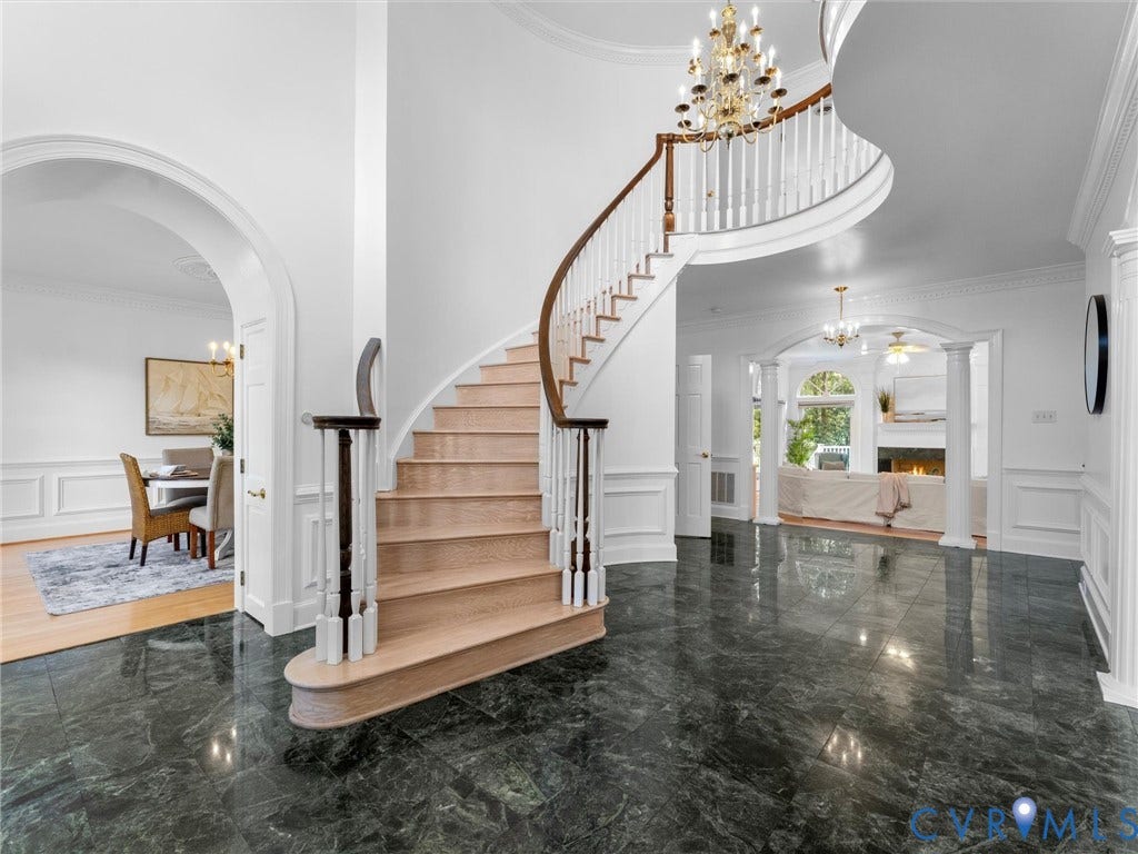 Grand foyer featuring a curved staircase with wood treads, white risers, and a wrought iron and wood railing