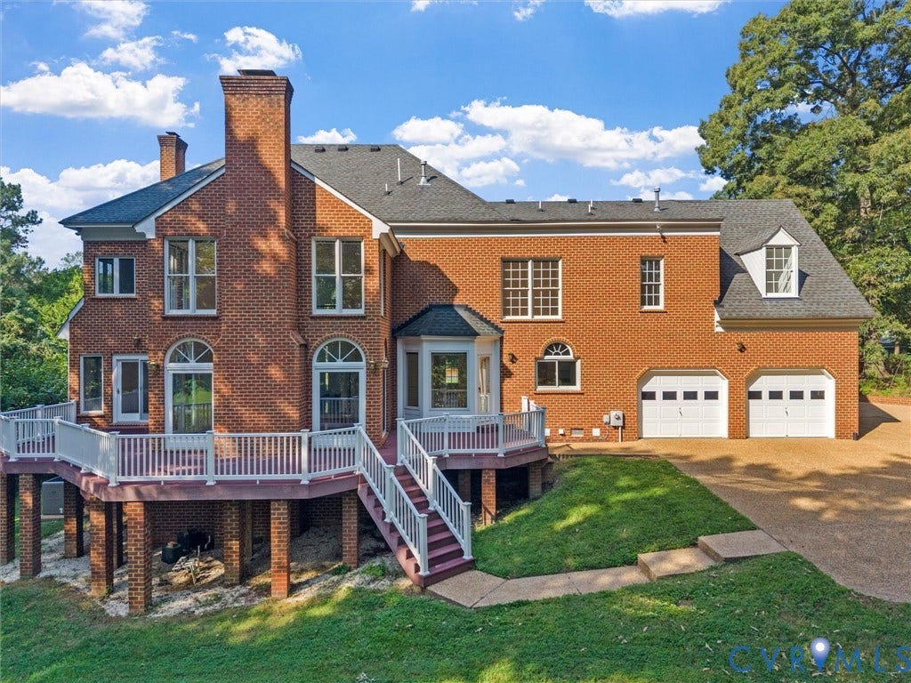 Brick exterior, multi-level deck with white railings, two-car garage, multiple large windows, and a bay window