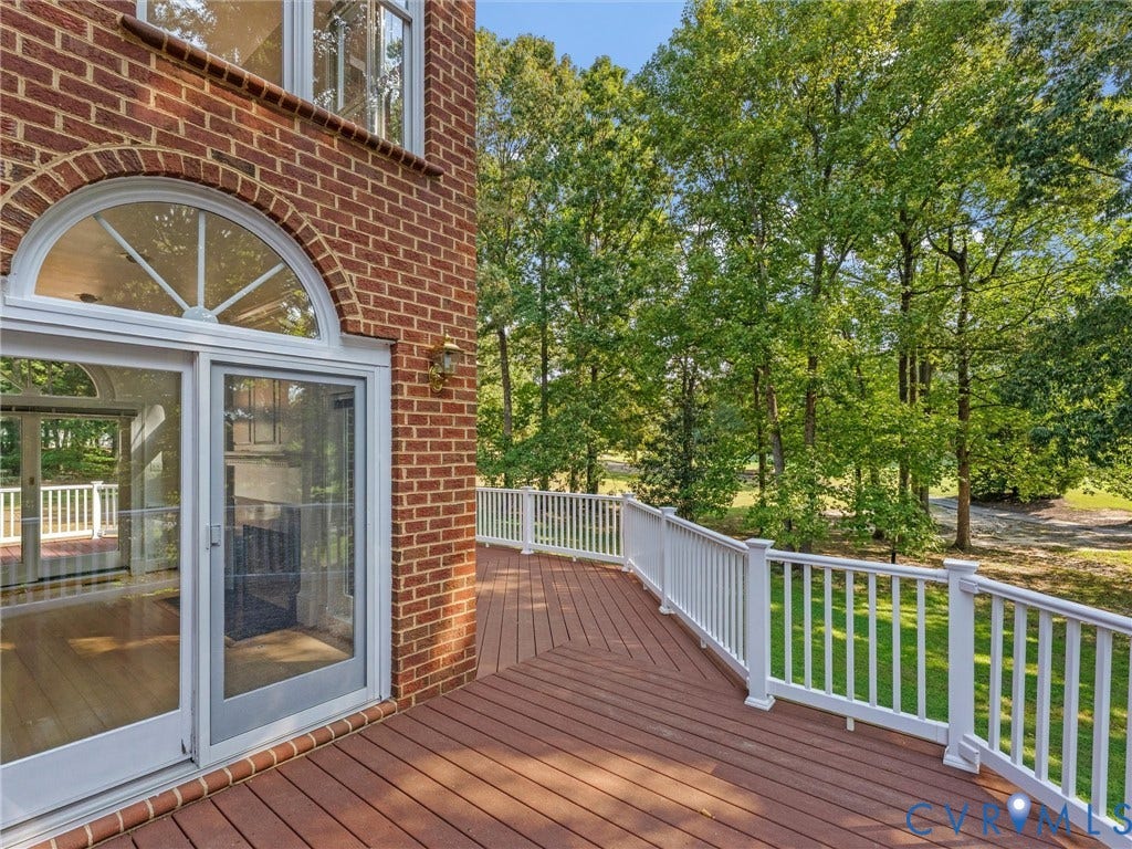 Expansive wood-finish deck with white railing, red brick exterior, and arched transom window