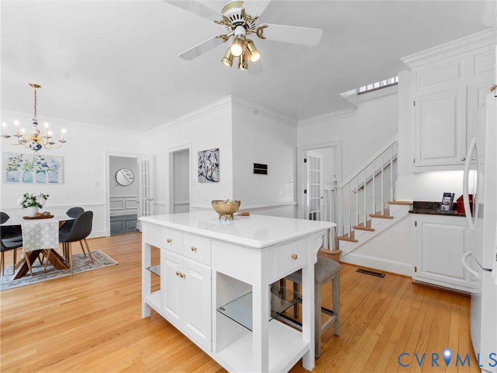 Kitchen island with integrated shelving, wood-finish flooring, white cabinetry, and granite countertops