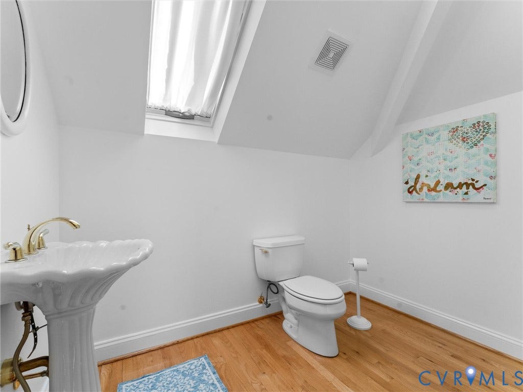 Pedestal sink with brass-finish faucet, wood-finish flooring, and sloped ceiling with skylight