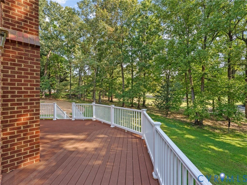 Expansive deck with composite decking and white railings, complemented by a brick exterior wall and a treed backdrop