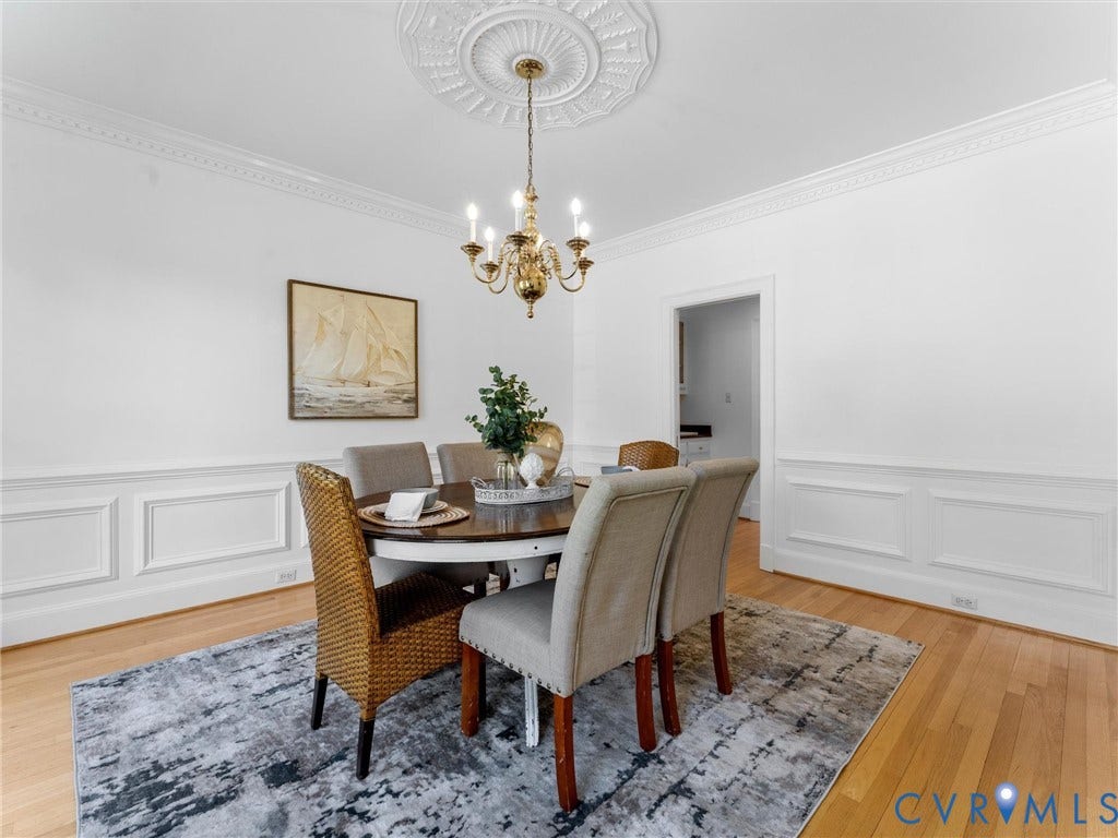Hardwood flooring, decorative crown molding, wainscoting, and a ceiling medallion with a chandelier