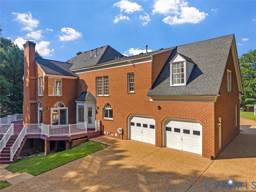Brick exterior with a multi-level deck, attached two-car garage, dormer window, and a prominent brick chimney