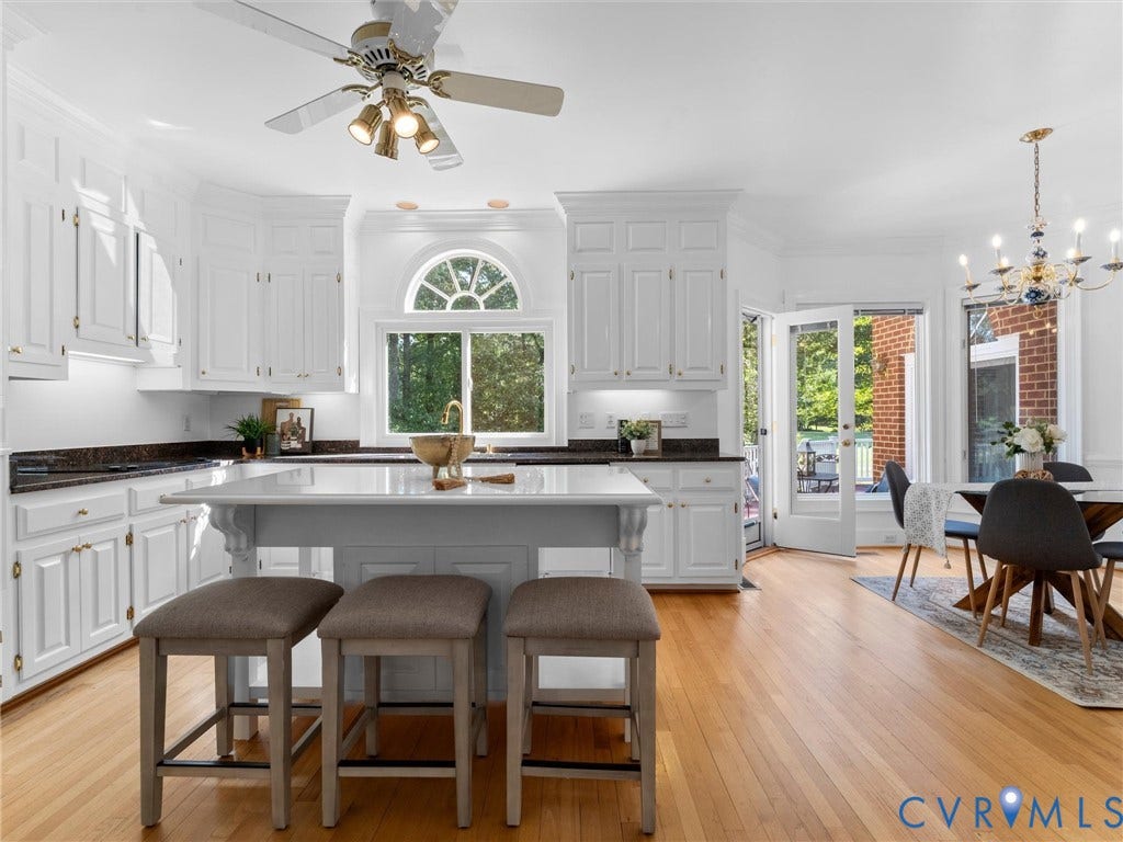 White cabinetry with gold-tone hardware, dark stone countertops, central island, light wood-finish flooring, and a decorative arched window