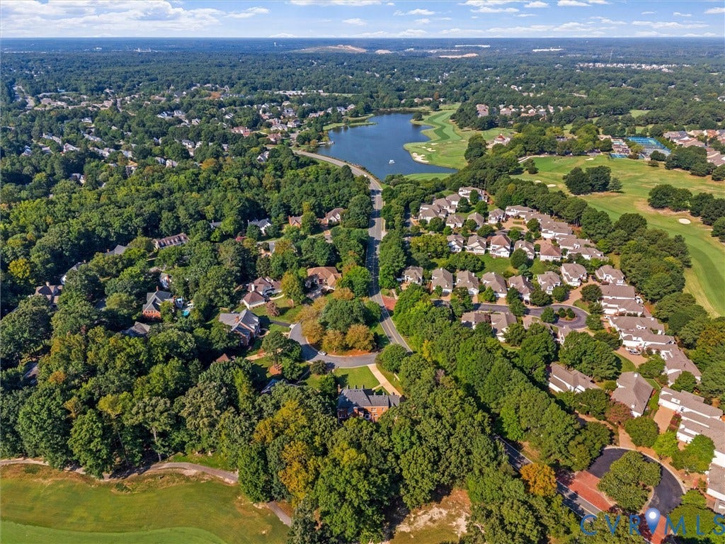 Aerial perspective of a verdant residential area featuring mature tree canopies, golf course access, and a prominent lake