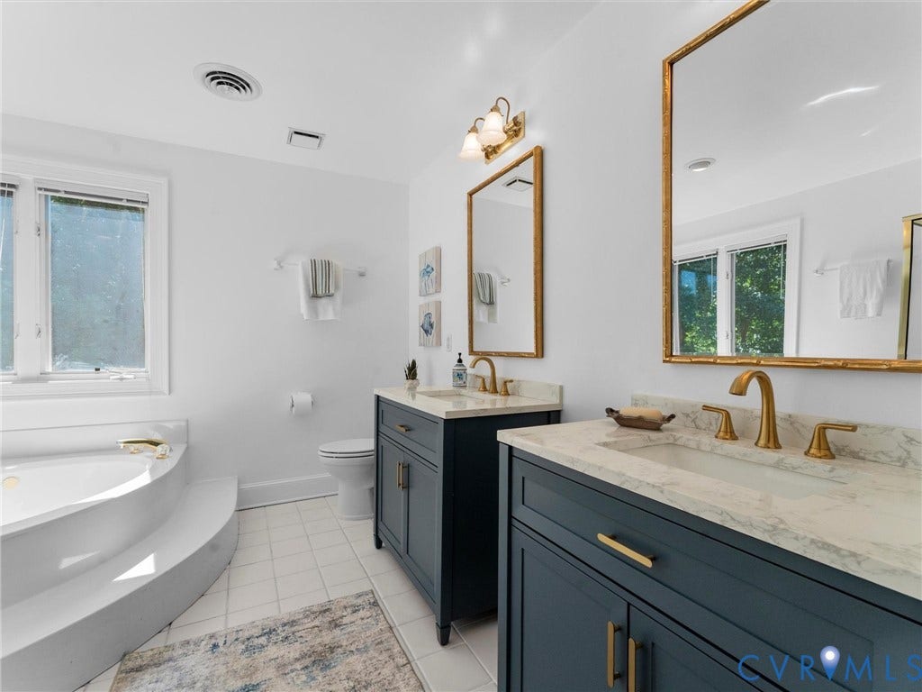 Dual vanities with stone countertops, individual gold-framed mirrors, gold-finish fixtures, and a built-in soaking tub