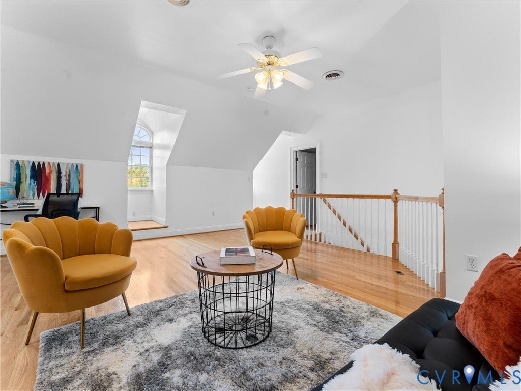 Bright attic space featuring wood-finish flooring, a ceiling fan with integrated lighting, and a dormer window with an arched transom