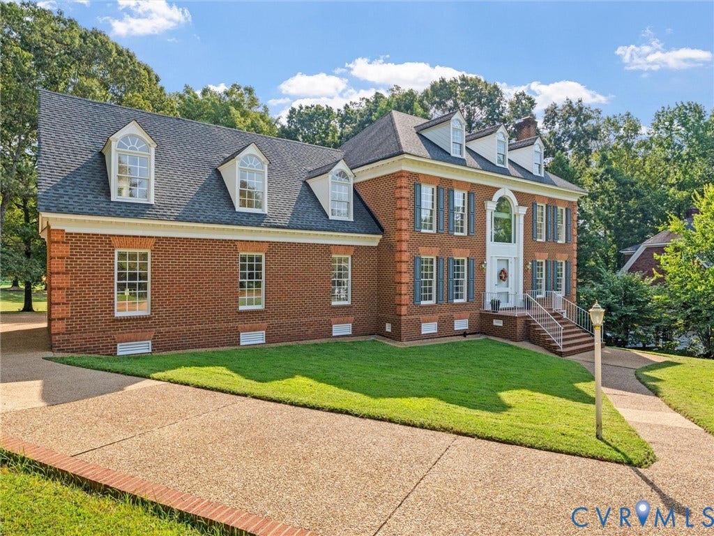 Brick exterior with dormer windows, a prominent entryway, a paved driveway, and manicured landscaping