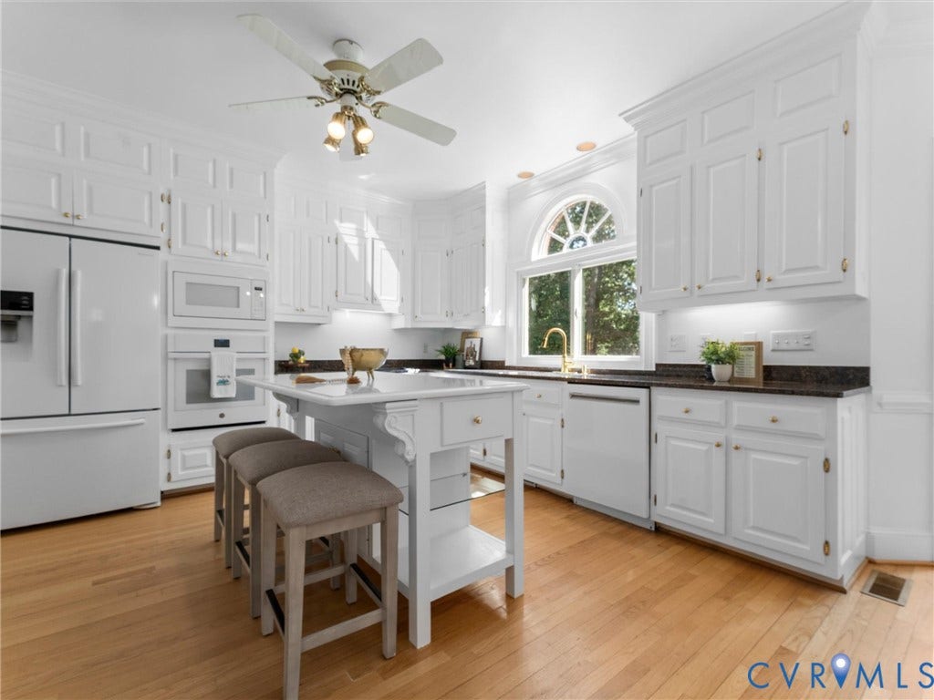 Bright kitchen featuring white cabinetry, dark countertops, a central island, wood-finish flooring, and an arched window