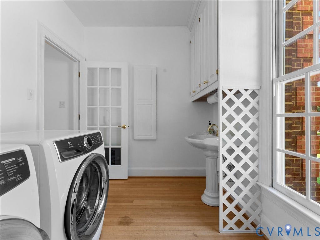 Utility area with wood-finish flooring, white cabinetry, a pedestal sink, and a multi-pane window
