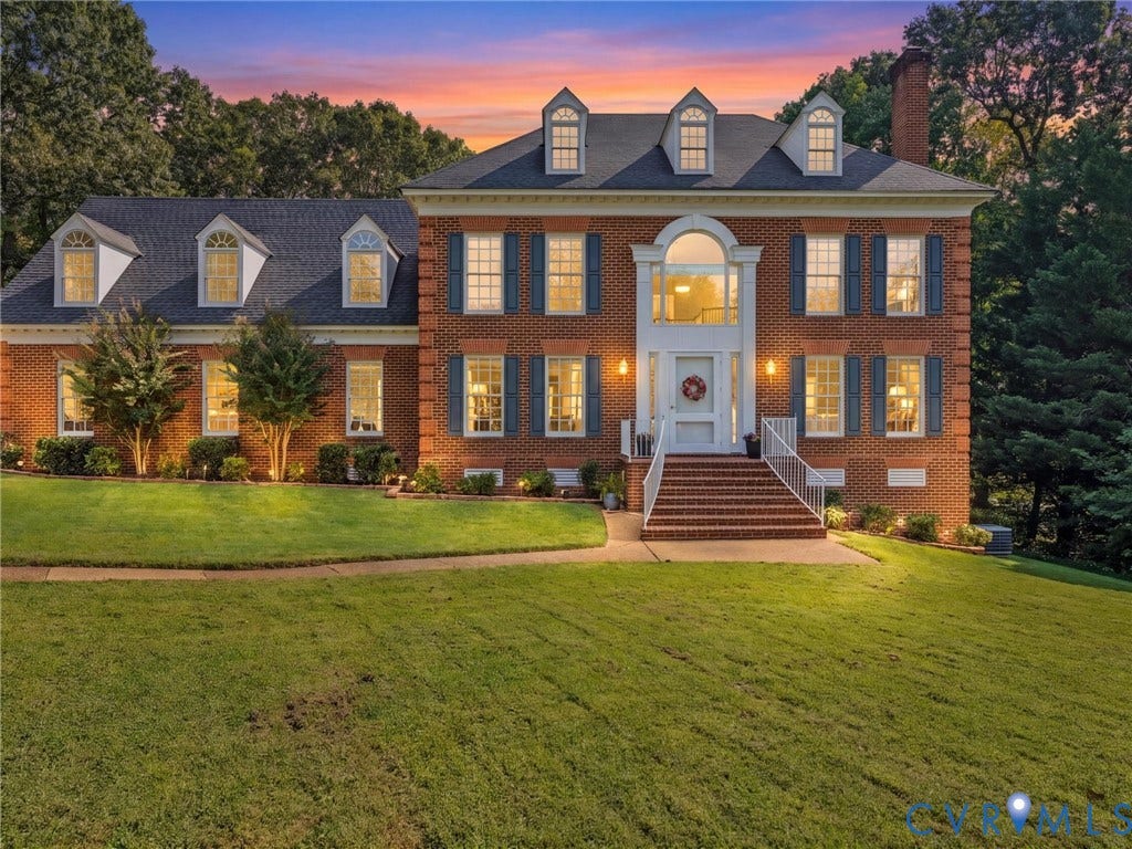 Brick colonial residence featuring a symmetrical facade, multiple dormer windows, a prominent arched entry, and a spacious front lawn