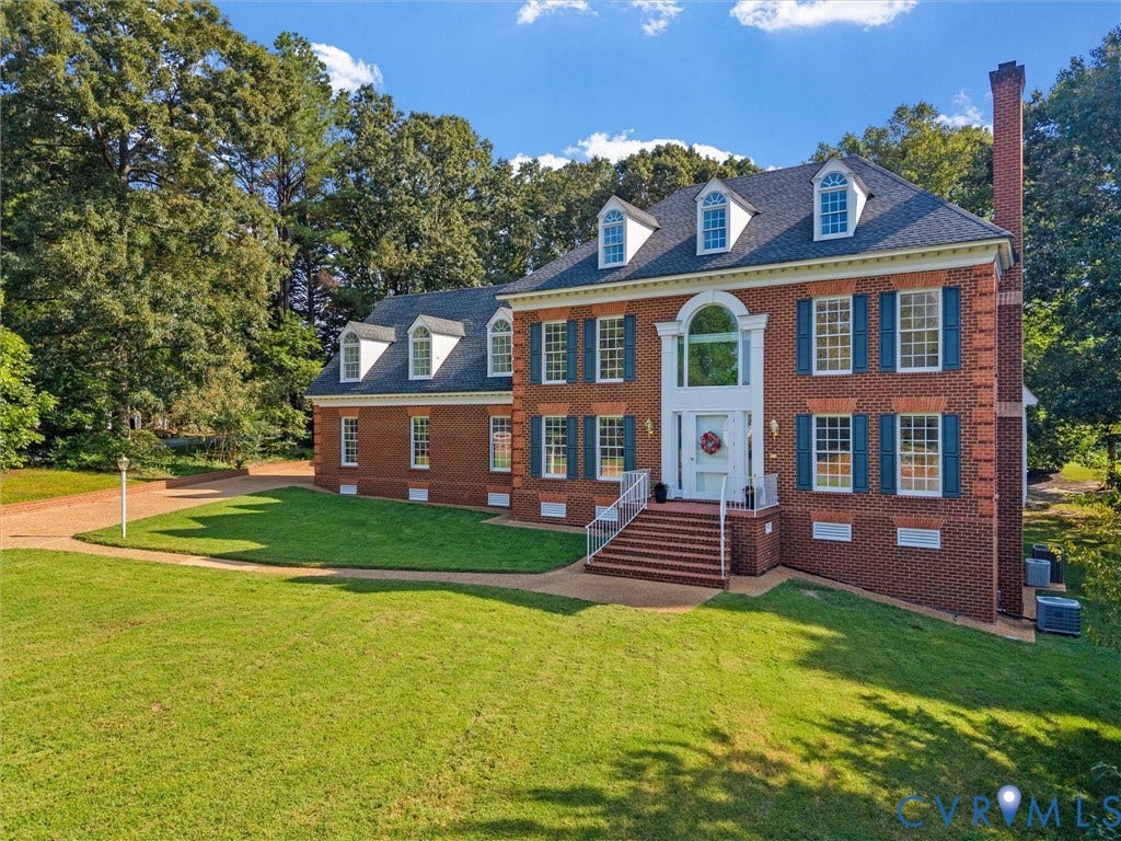Brick-front exterior with multiple dormer windows, a prominent arched window above the entry, a brick chimney, and a landscaped lawn