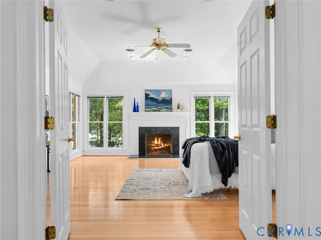 Vaulted ceiling, ceiling fan, recessed lighting, wood-finish flooring, and a fireplace with a dark stone surround and white mantel