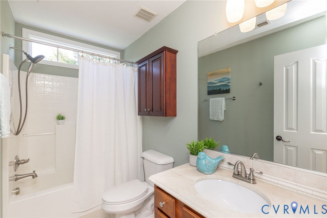 12669 Fawn Lane, Goochland, VA 23233 Full bathroom featuring a white tub/shower combination with tile surround, a built-in wood-finish cabinet, and a single vanity with a solid surface countertop