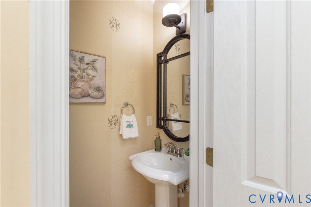 12669 Fawn Lane, Goochland, VA 23233 Pedestal sink with chrome fixtures, an arched mirror, and a wall-mounted light fixture