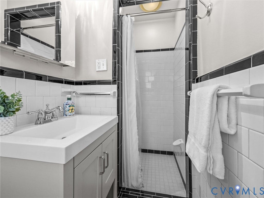 600 Baldwin Road, Henrico, VA 23229 Tiled shower stall with a glass enclosure, white subway tile walls, black accent tiling, and a gray vanity with an integrated sink