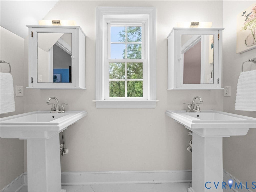 600 Baldwin Road, Henrico, VA 23229 Two pedestal sinks with chrome fixtures, framed window, two mirrored medicine cabinets, and wall-mounted lighting