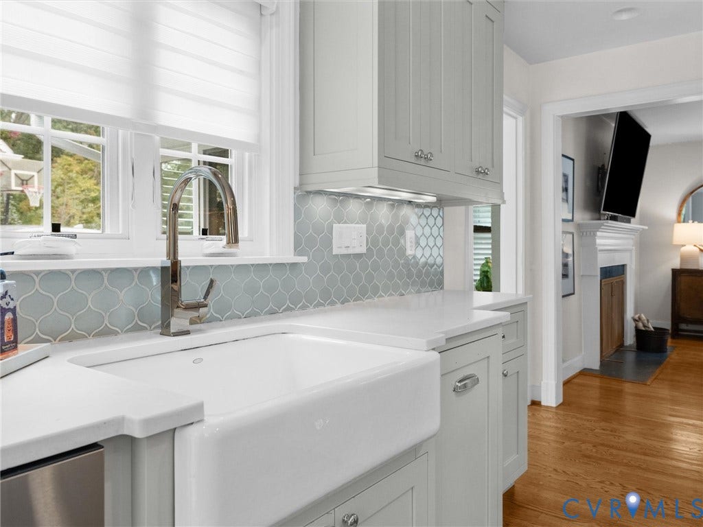 600 Baldwin Road, Henrico, VA 23229 White farmhouse sink with a gooseneck faucet, light blue arabesque tile backsplash, light-toned cabinetry, white countertops, and hardwood flooring