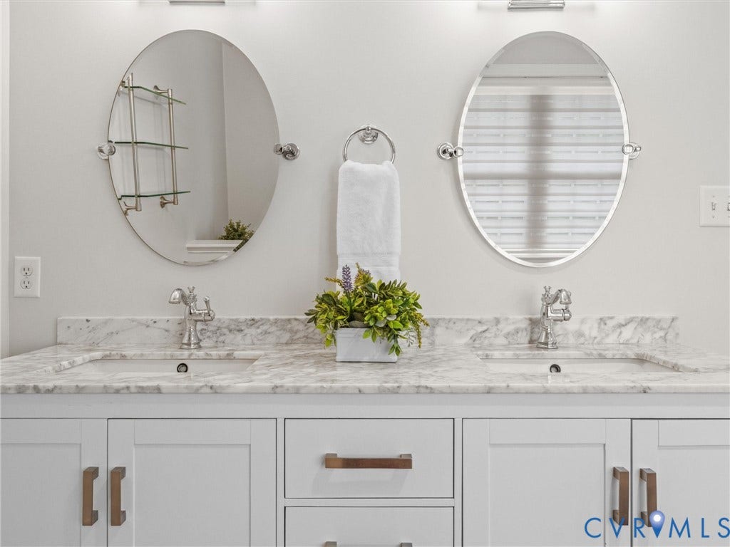 600 Baldwin Road, Henrico, VA 23229 Dual oval mirrors, white shaker-style cabinetry, double undermount sinks, and stone countertops