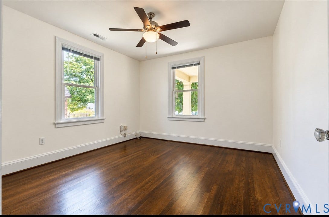 Rich wood-finish flooring, two large windows, a ceiling fan with integrated lighting, and white trim