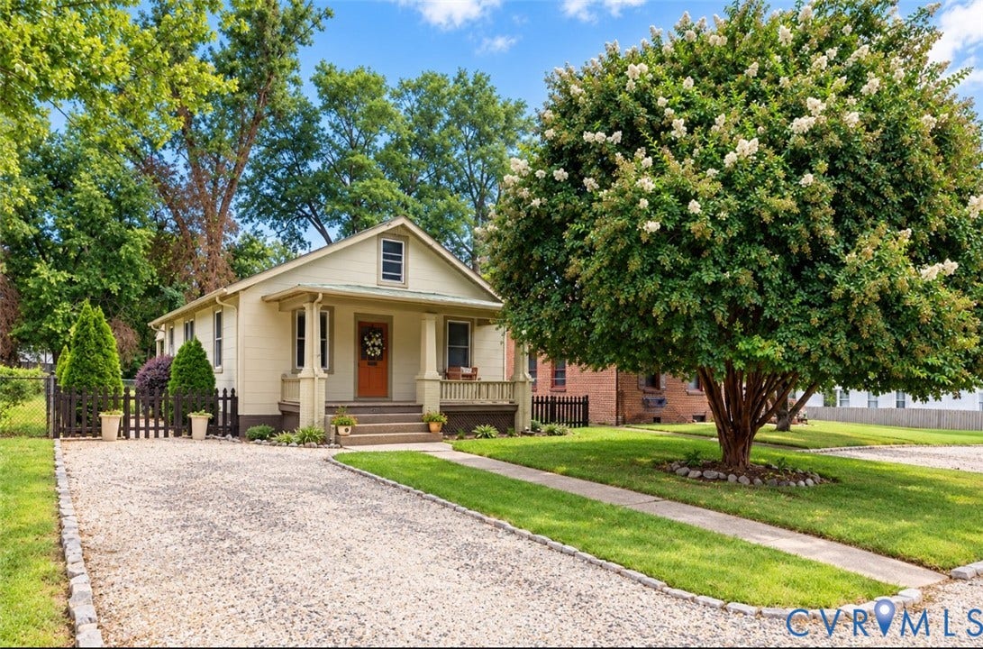 Light-toned exterior, covered porch, green metal accent roof, with an apricot colored front door and matching swing. Stunning 34 year old Crpe Myrtle!