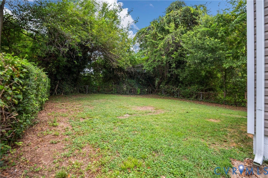 2211 Royall Avenue, Bellemeade, Richmond, VA 23224 Expansive grassy area bordered by mature foliage, featuring a dense green hedge and partial vinyl siding